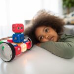 Precision Robotics - boy lying on bed playing with red and blue toy truck